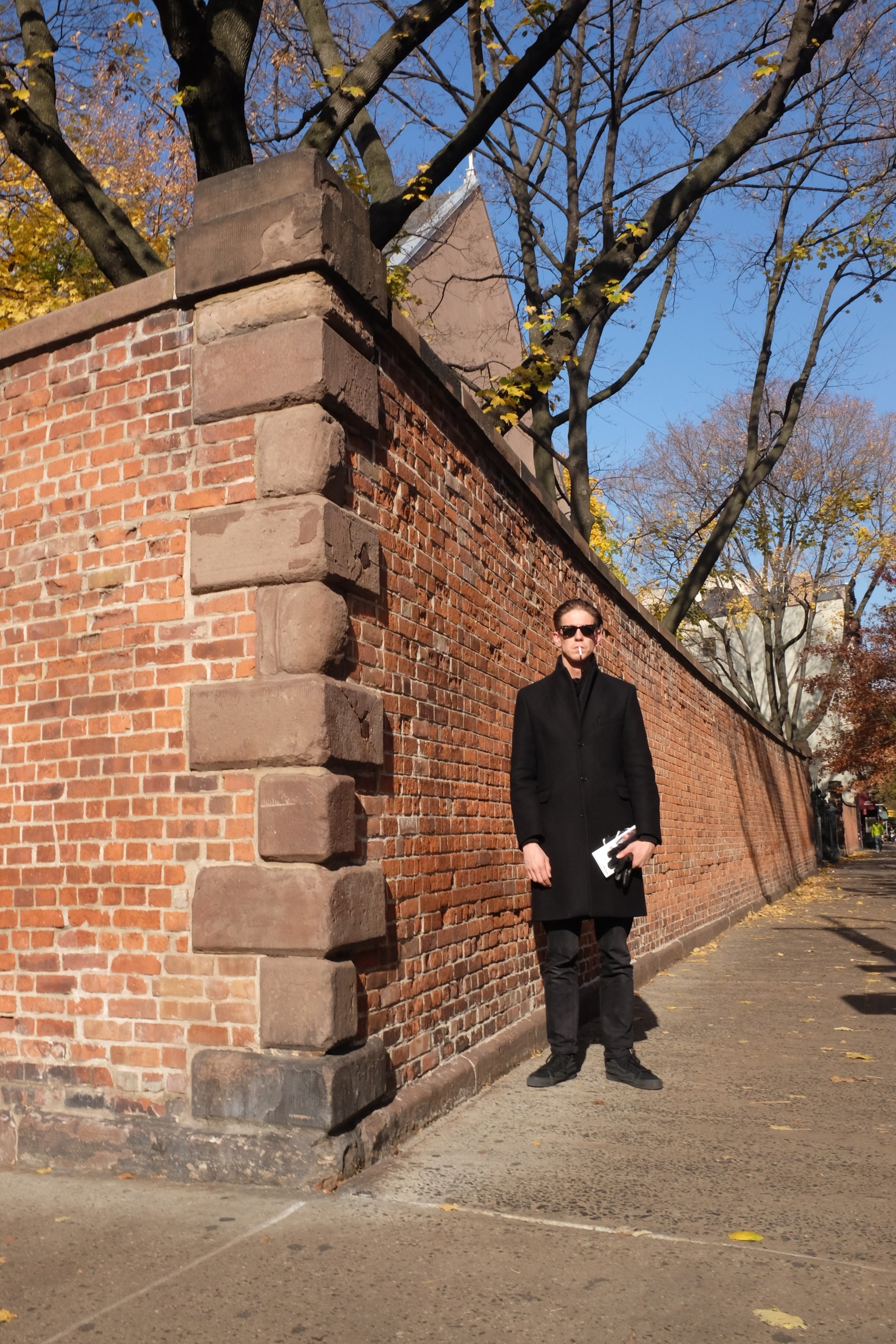 man in black standing by brick wall